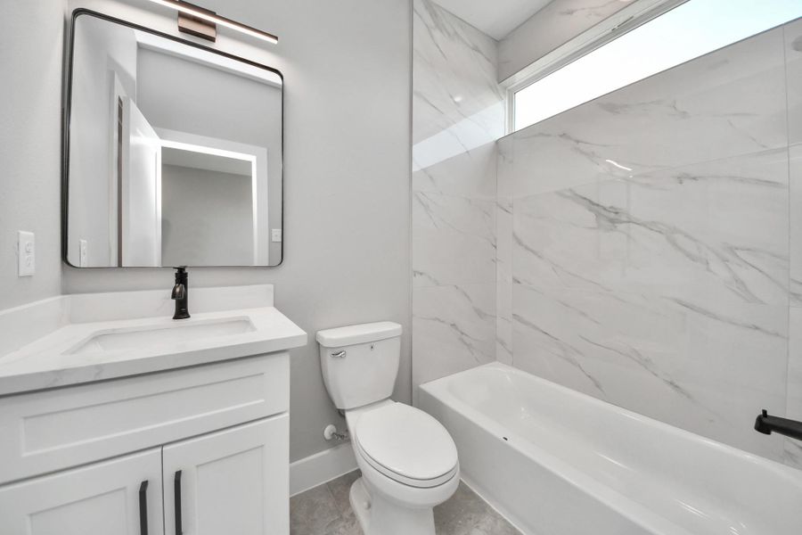 Stylish guest bathroom featuring modern fixtures, quartz countertops, & sleek marble-look tile surround for a clean contemporary feel.