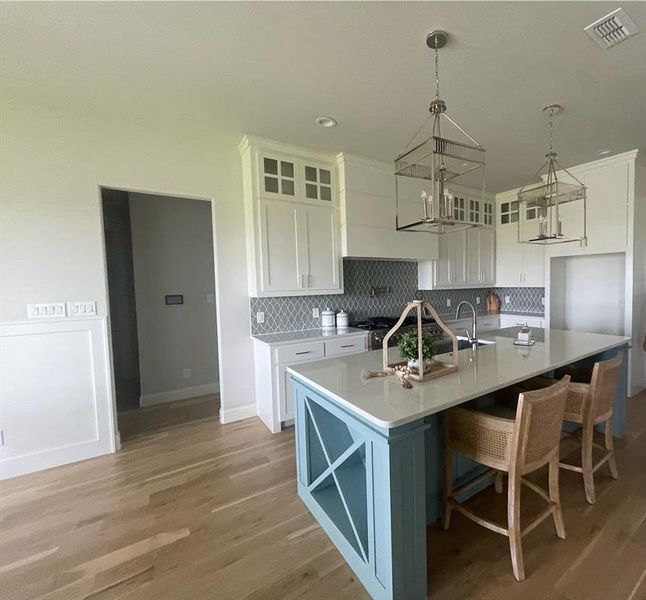 Kitchen featuring white cabinets, a chandelier, a kitchen island with sink, tasteful backsplash, and light wood-style floors Kitchen featuring white cabinets, a chandelier, a kitchen island with sink, tasteful backsplash, and light wood-style floors