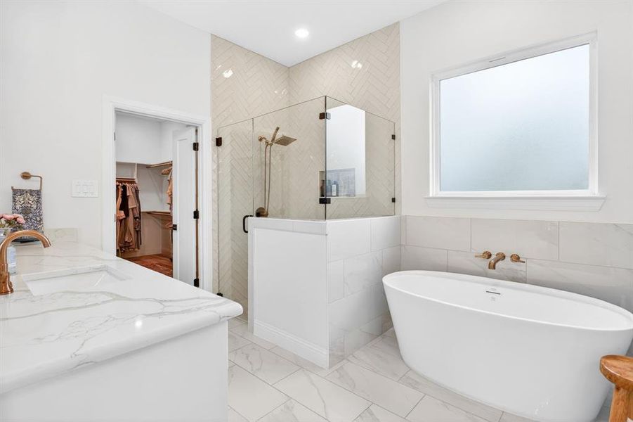 Full bath featuring a stall shower, vanity, a walk in closet, a soaking tub, and light marble finish flooring Full bath featuring a stall shower, vanity, a walk in closet, a soaking tub, and light marble finish flooring