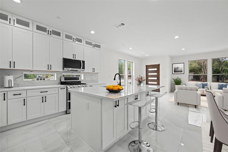 Kitchen featuring an island with sink, appliances with stainless steel finishes, white cabinetry, and decorative backsplash