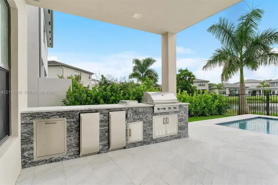 Covered patio featuring an outdoor kitchen with stainless steel appliances, stone-patterned cabinetry, stone countertops, and a swimming pool