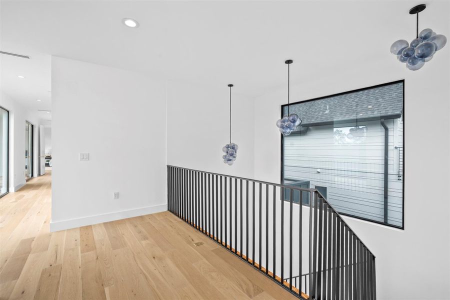 An open landing area featuring light wood flooring, white walls, and contemporary pendant lighting fixtures