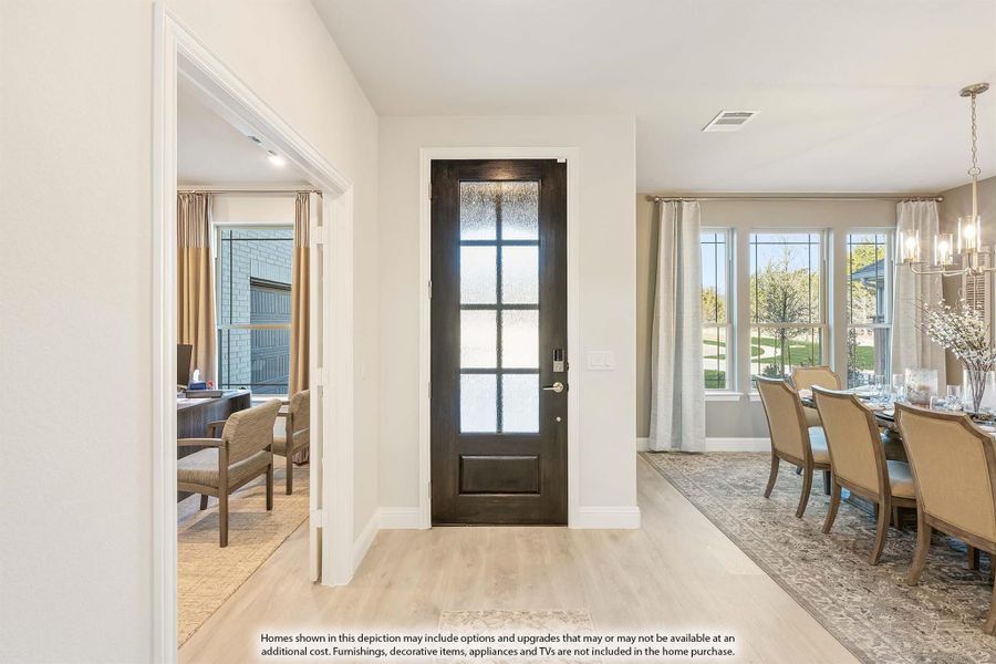 Entryway with dark wood front door, light hardwood floors, and dining room with chandelier visible to the right.