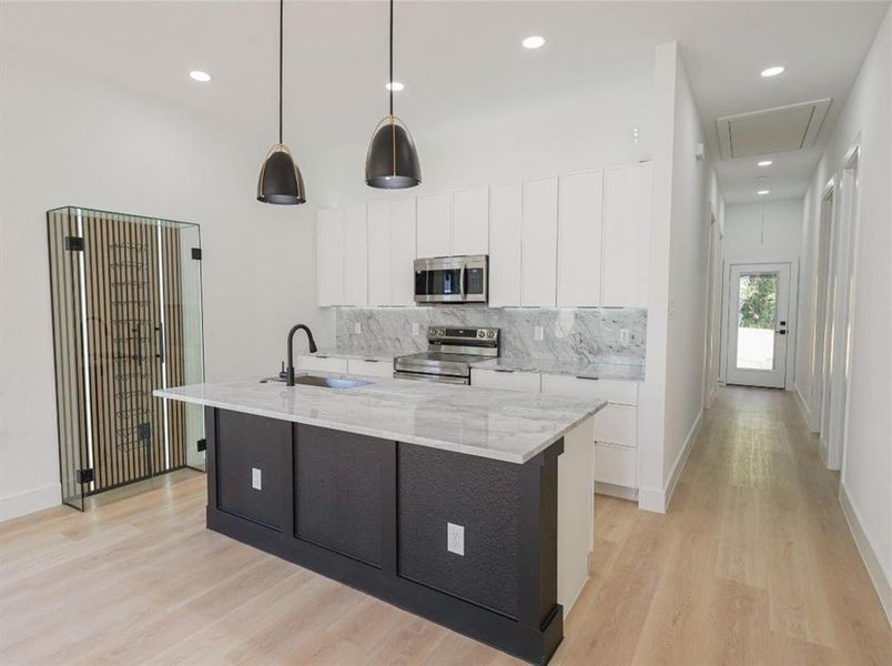 Kitchen with tasteful backsplash, stainless steel appliances, white cabinetry, light stone counters, and a kitchen island with sink Kitchen with tasteful backsplash, stainless steel appliances, white cabinetry, light stone counters, and a kitchen island with sink