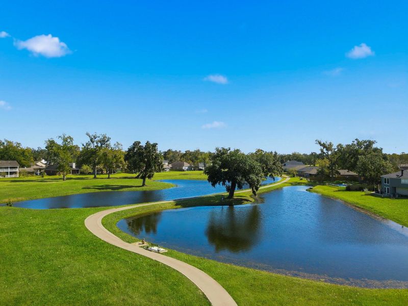 A peaceful scene of the Columbia Lakes community lagoons, surrounded by lush greenery and mature trees. The winding walking paths invite residents to enjoy morning strolls or sunset walks while taking in the reflection of nature on the calm waters — a perfect blend of serenity and resort-style living.