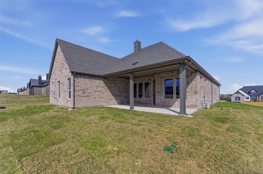 Rear view of property featuring brick siding, a lawn, a patio, and a chimney
