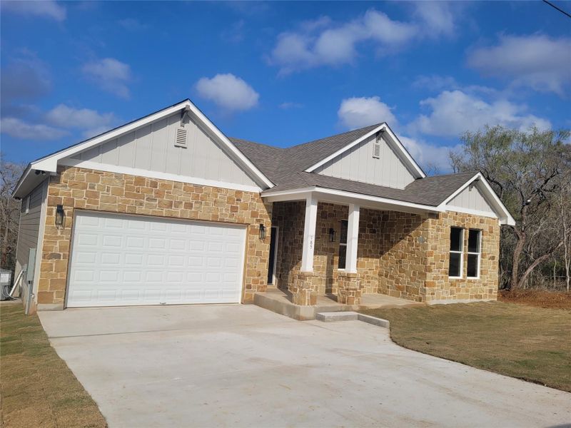 View of front of house featuring covered porch, stone siding, a front yard, and driveway