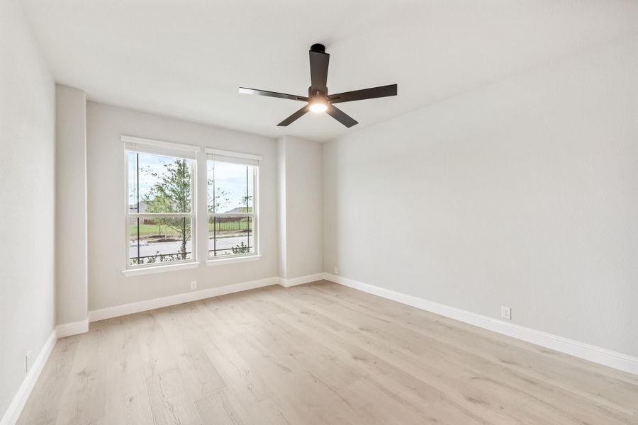 Empty room with light hardwood floors, black ceiling fan, and two windows with outdoor views