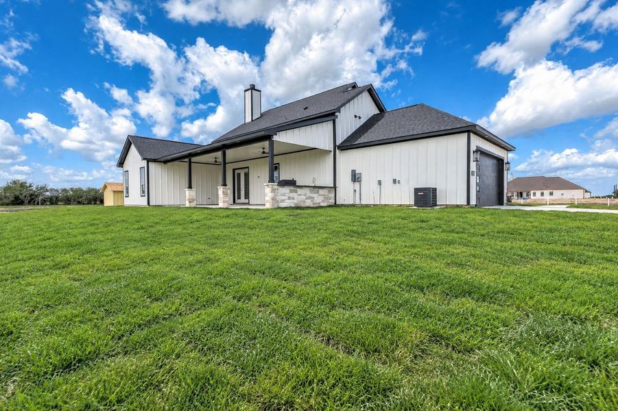 Rear view of the home showcasing the covered patio, outdoor kitchen area, spacious backyard, and side-entry garage.