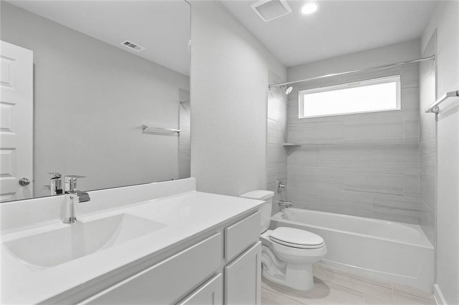 Secondary bath features tile flooring, bath/shower combo with tile surround, stained wood cabinets, beautiful light countertops, mirror, sleek fixtures and modern finishes.