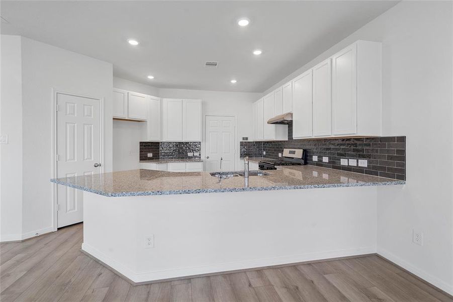 This spacious kitchen features high ceilings, stained wood cabinets, granite countertops, SS appliances, modern tile backsplash, recessed lighting, space for a breakfast bar, and a pantry all overlooking your huge family room.