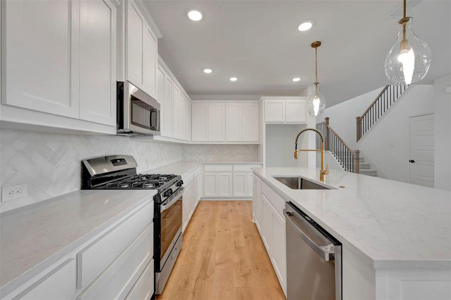 Kitchen with stainless steel appliances, white cabinets, a kitchen island with sink, decorative light fixtures, and light wood-type flooring