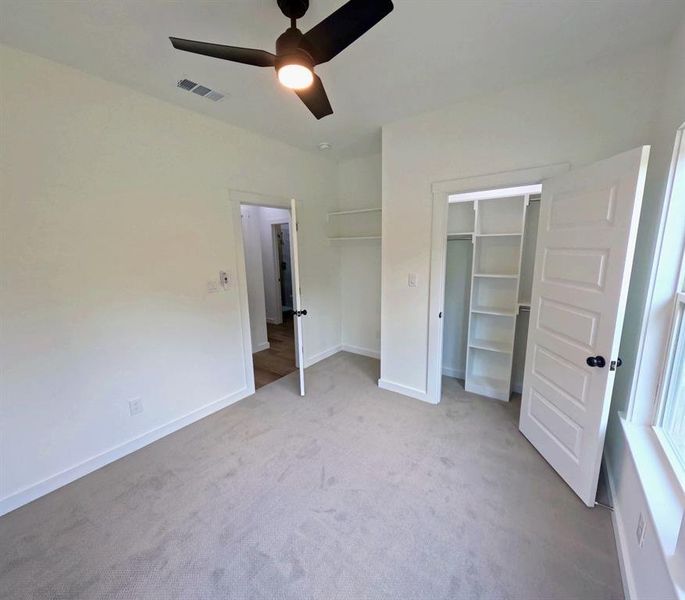 Unfurnished bedroom with carpet floors, a ceiling fan, and a walk in closet Unfurnished bedroom with carpet floors, a ceiling fan, and a walk in closet