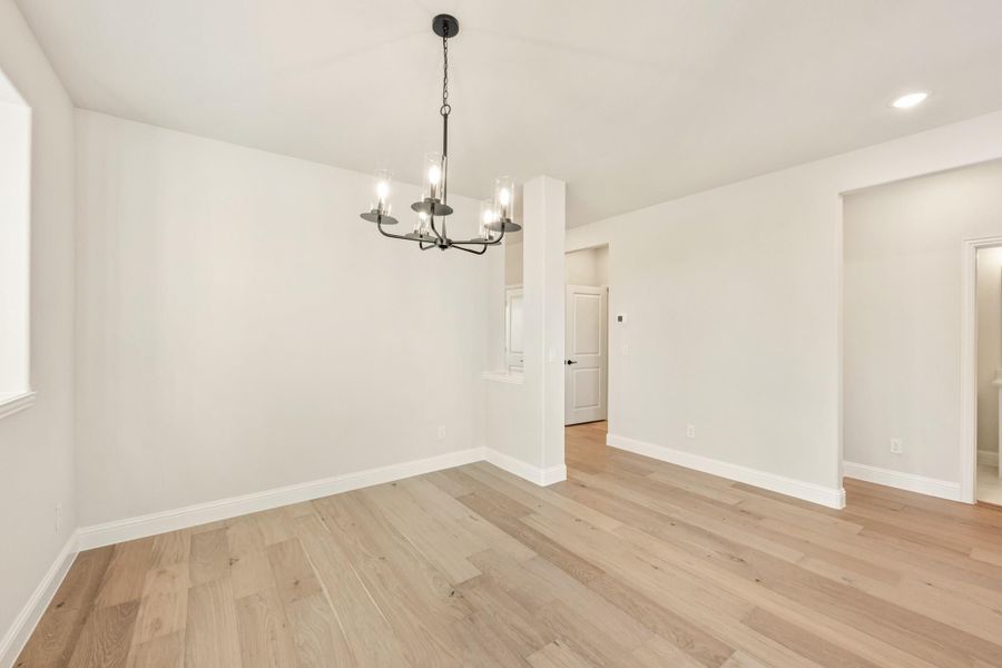 Empty dining room with light hardwood floors, white walls, and a black metal chandelier