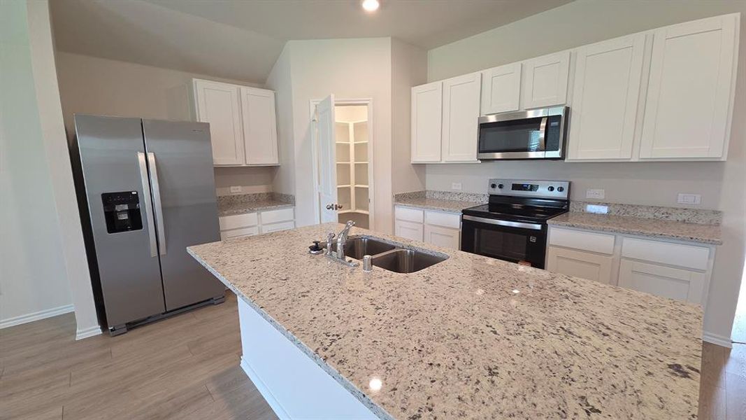 Kitchen featuring a central island with a double basin sink, light-colored granite countertops, white cabinetry, stainless steel appliances, and wood-finish flooring