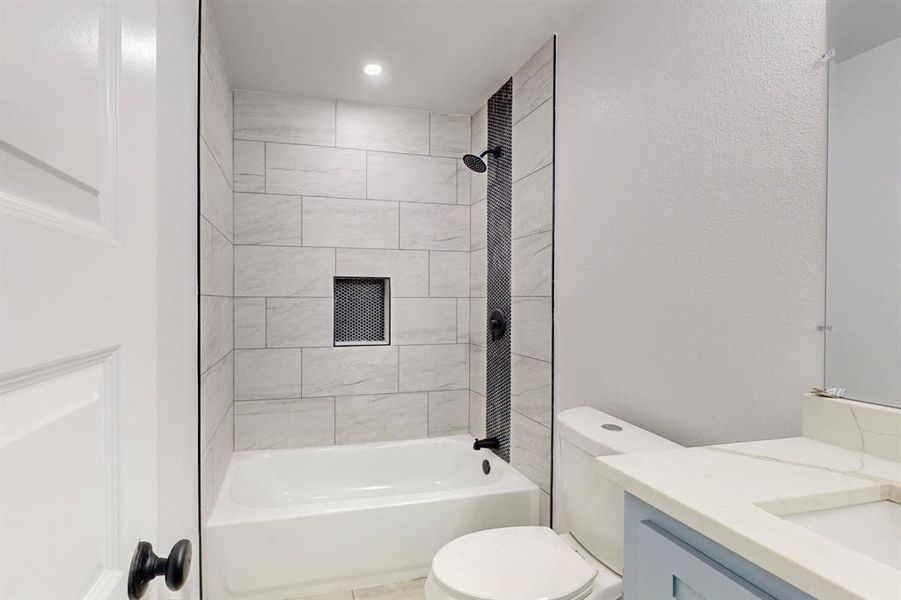 Full bathroom with tiled shower / bath combo, toilet, and vanity