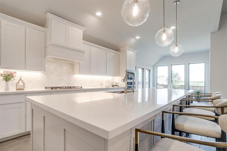 Kitchen featuring a sink, backsplash, a kitchen island with sink, light countertops, and vaulted ceiling Kitchen featuring a sink, backsplash, a kitchen island with sink, light countertops, and vaulted ceiling