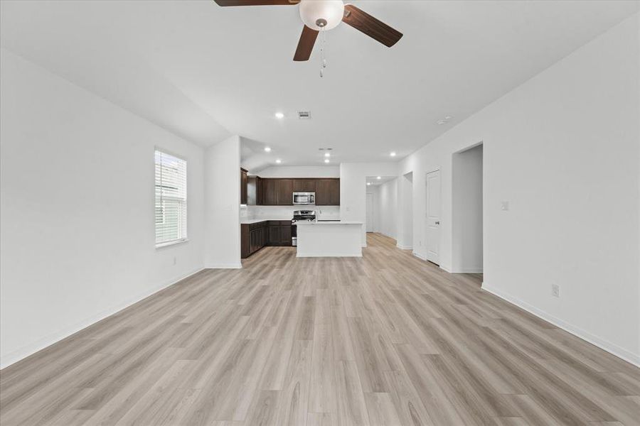 Unfurnished living room with light hardwood / wood-style floors, vaulted ceiling, and ceiling fan