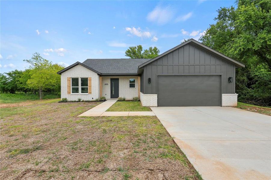 View of front facade with brick siding, board and batten siding, an attached garage, driveway, and a shingled roof