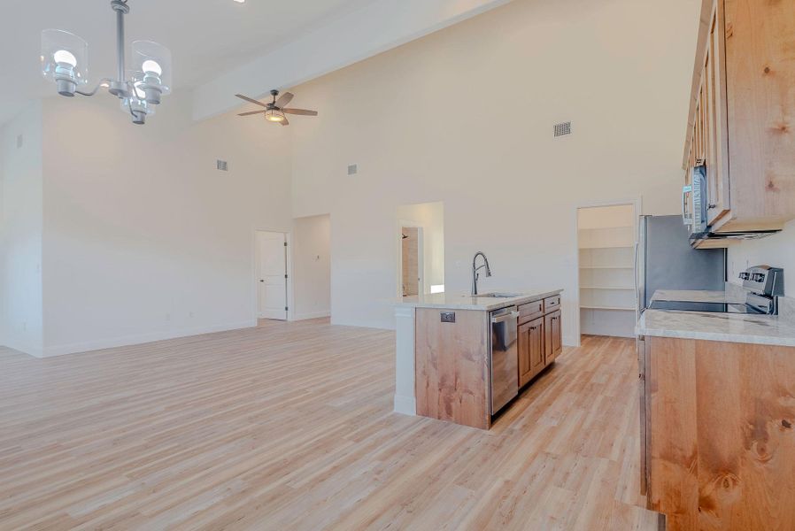 Kitchen with a chandelier, light wood-style floors, an island with sink, light brown cabinetry, and decorative light fixtures Kitchen with a chandelier, light wood-style floors, an island with sink, light brown cabinetry, and decorative light fixtures