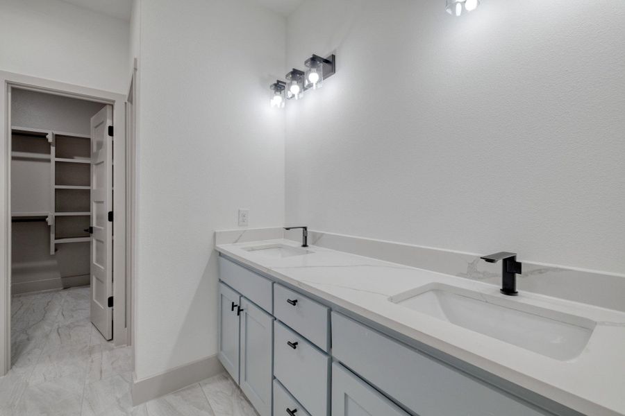 Full primary bath featuring double vanity, light marble finish floors, and a walk in closet Full primary bath featuring double vanity, light marble finish floors, and a walk in closet