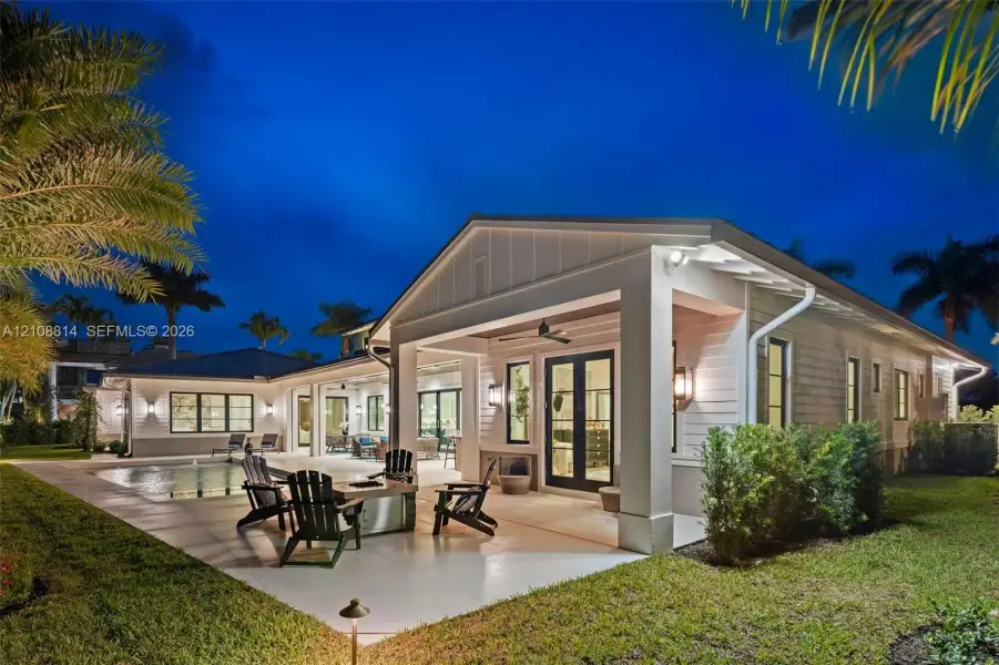 Covered rear terrace featuring a concrete patio, integrated ceiling fan, and wall-mounted exterior lighting, complemented by a swimming pool and board-and-batten siding Covered rear terrace featuring a concrete patio, integrated ceiling fan, and wall-mounted exterior lighting, complemented by a swimming pool and board-and-batten siding