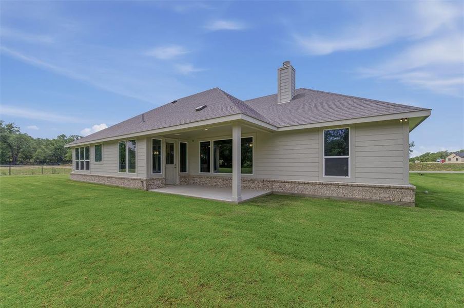 Expansive rear yard featuring a covered patio, neutral siding, stone veneer foundation, and a shingled roof with a chimney
