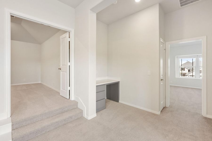 Carpeted bonus room with built-in desk, raised step area, and doorways leading to additional rooms Carpeted bonus room with built-in desk, raised step area, and doorways leading to additional rooms