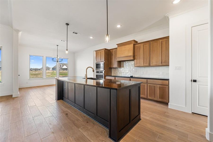 Kitchen with an island with sink, brown cabinetry, hanging light fixtures, light wood-style floors, and recessed lighting