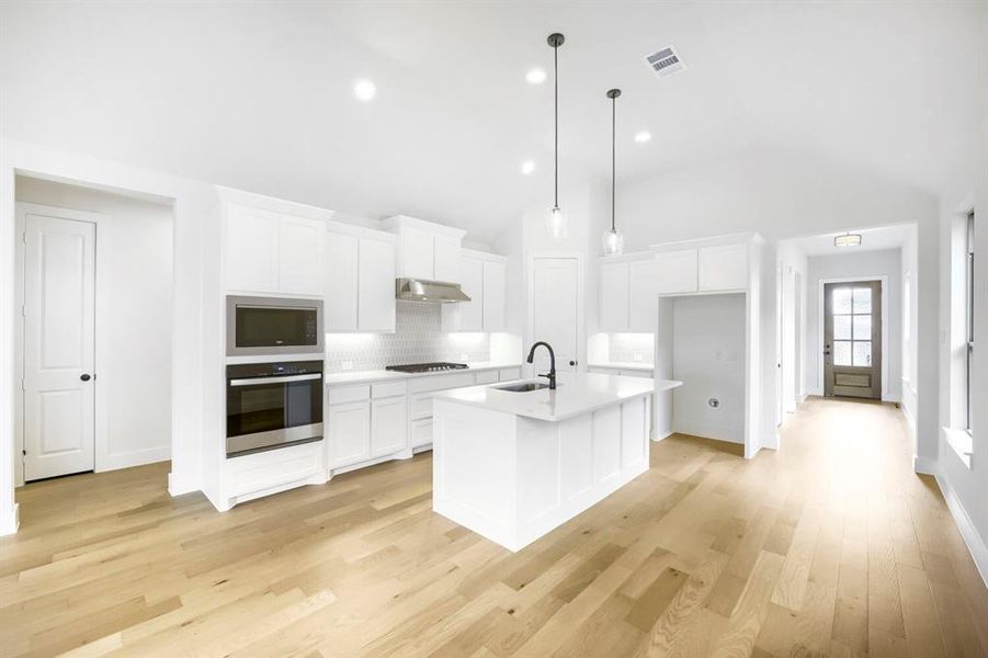 Modern kitchen featuring a central island, light wood-finish flooring, white cabinetry, integrated stainless steel appliances, and a tiled backsplash Modern kitchen featuring a central island, light wood-finish flooring, white cabinetry, integrated stainless steel appliances, and a tiled backsplash