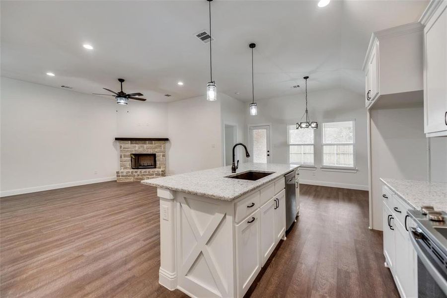 Kitchen featuring white cabinets, open floor plan, pendant lighting, a fireplace, and light stone counters