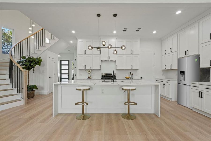 Kitchen featuring a breakfast bar area, light stone counters, light wood-style floors, a kitchen island with sink, and white cabinets