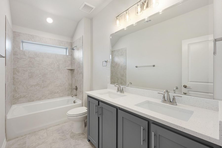 Bathroom with double sink vanity, gray cabinets, tiled tub-shower combo, and large mirror with overhead lighting Bathroom with double sink vanity, gray cabinets, tiled tub-shower combo, and large mirror with overhead lighting
