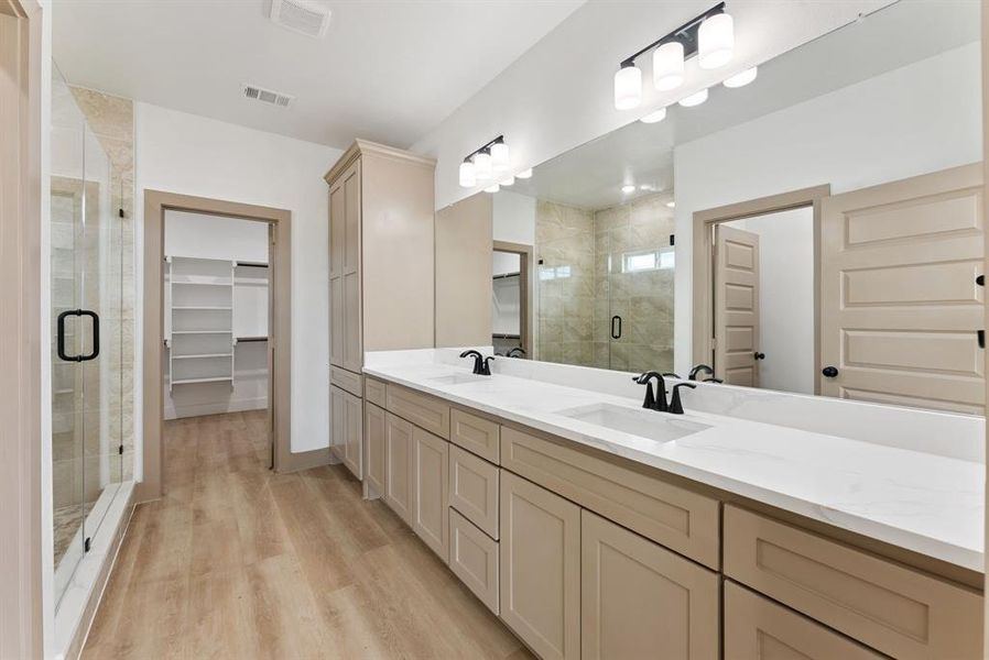 Bathroom with a walk in closet, double vanity, a shower stall, and light wood-style flooring Bathroom with a walk in closet, double vanity, a shower stall, and light wood-style flooring