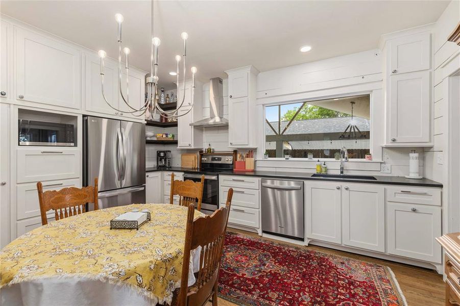 Kitchen featuring white shaker cabinetry, stainless steel appliances, dark countertops, a tile backsplash, and a large window