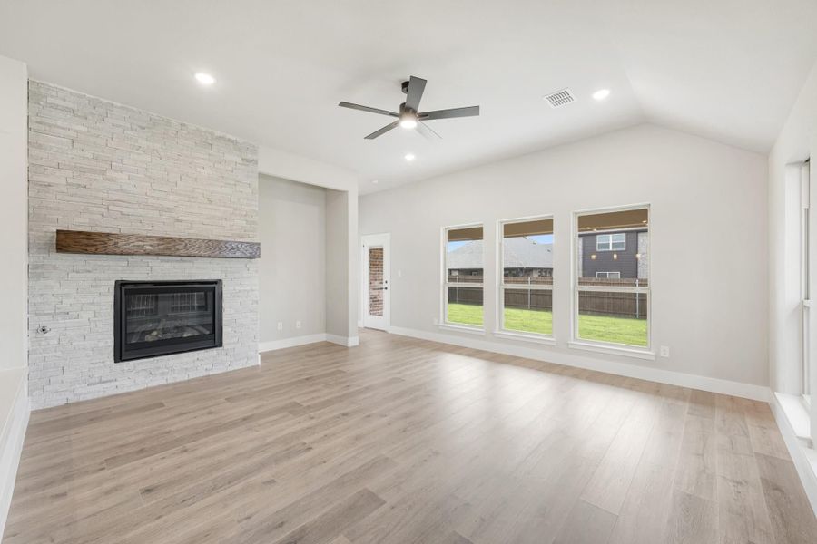Open living room with stone fireplace, wood mantel, vaulted ceiling, and light hardwood floors