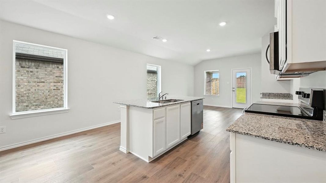 Open-concept kitchen featuring white cabinetry, light granite countertops, stainless steel appliances, a central island with sink, and wood-finish flooring Open-concept kitchen featuring white cabinetry, light granite countertops, stainless steel appliances, a central island with sink, and wood-finish flooring
