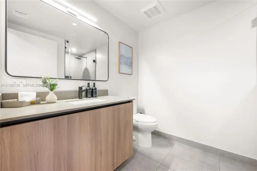 Floating wood-finish vanity with a stone countertop, integrated sink, matte black faucet, and large rectangular mirror with integrated lighting Floating wood-finish vanity with a stone countertop, integrated sink, matte black faucet, and large rectangular mirror with integrated lighting