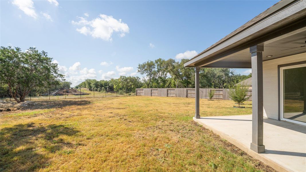 Fenced backyard featuring a patio and view of scattered trees Fenced backyard featuring a patio and view of scattered trees