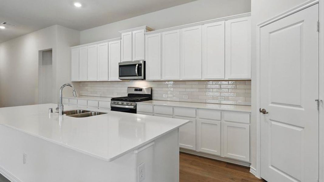 Modern kitchen featuring an expansive island with an undermount dual-basin sink, white shaker-style cabinetry, a subway tile backsplash, and stainless steel appliances including an oven range and microwave