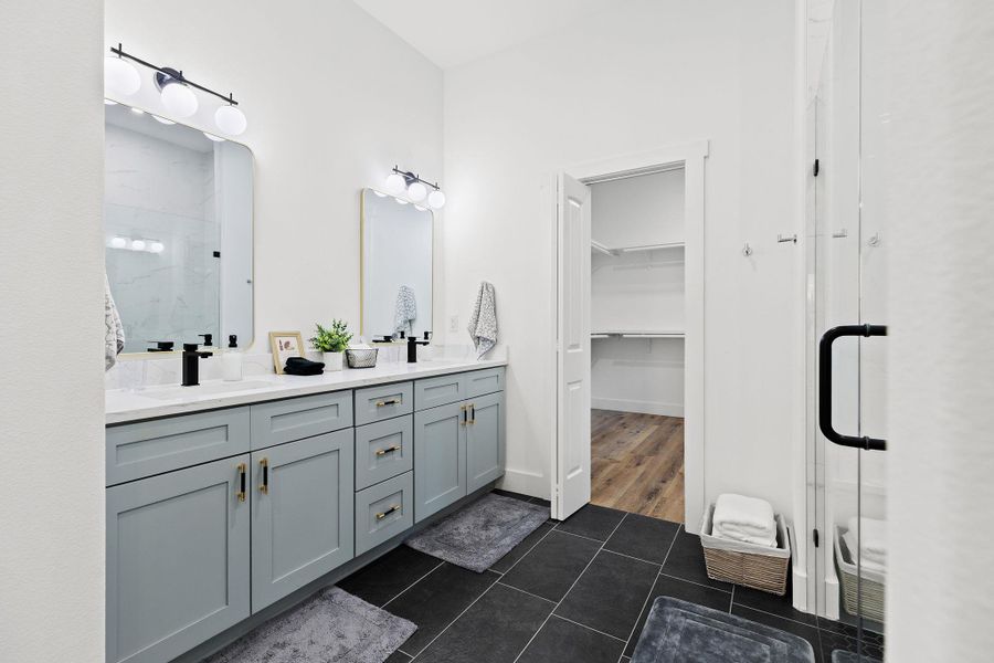 Full bathroom with a stall shower, double vanity, a spacious closet, and dark tile patterned floors