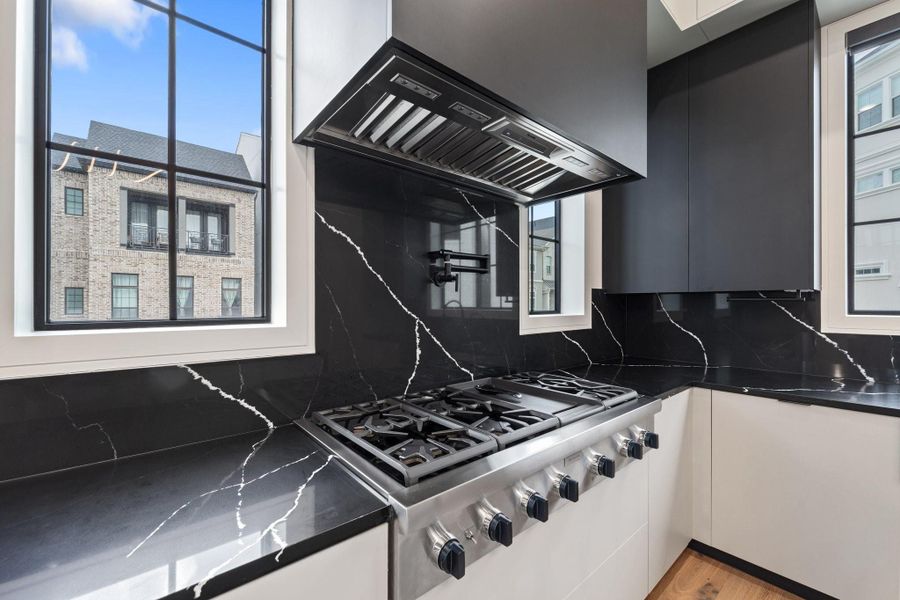 This modern kitchen showcases a sleek Thermador gas stove with multiple burners, set against elegant black marble countertops and a matching backsplash. Large windows flood the space with natural light, enhancing the clean, contemporary design. This modern kitchen showcases a sleek Thermador gas stove with multiple burners, set against elegant black marble countertops and a matching backsplash. Large windows flood the space with natural light, enhancing the clean, contemporary design.