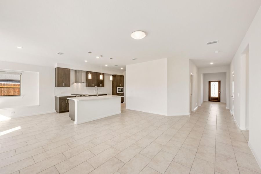 Open-concept kitchen with dark wood cabinets, white island, and tile floors leading to a hallway