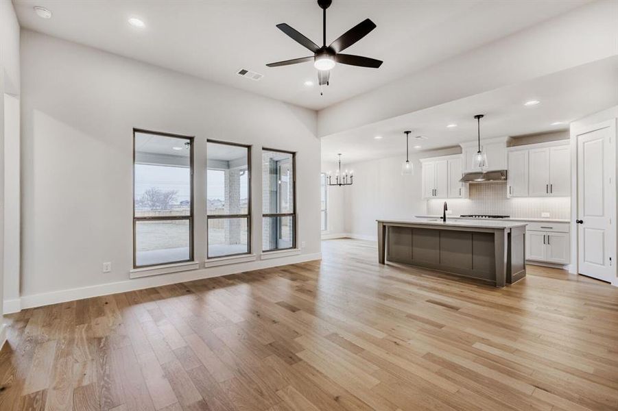 Kitchen with a ceiling fan, open floor plan, a chandelier, a center island with sink, and light countertops