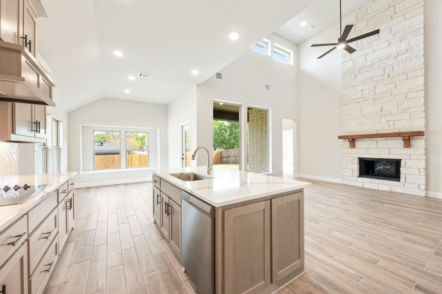 Open kitchen with island sink, vaulted ceiling, and stone fireplace in adjoining living area