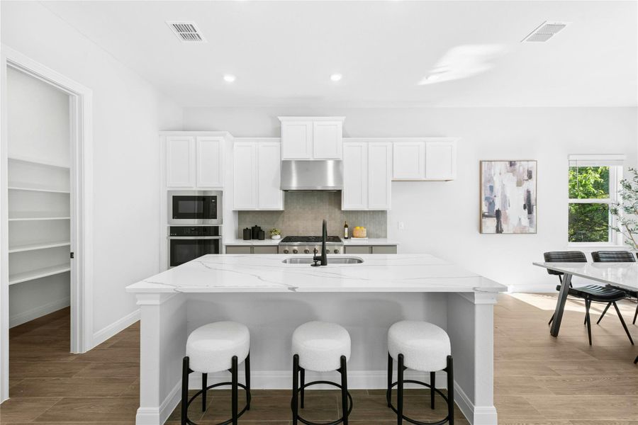 Kitchen with white cabinets, backsplash, a kitchen breakfast bar, light wood-type flooring, and light quartz counters Kitchen with white cabinets, backsplash, a kitchen breakfast bar, light wood-type flooring, and light quartz counters