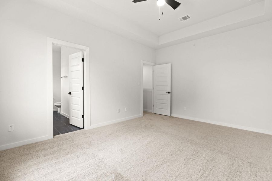 A spacious, neutral-toned room with plush carpeting and a modern ceiling fan offers comfort and tranquility.
