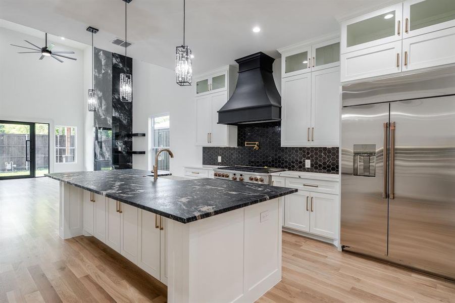 Kitchen with white cabinetry, appliances with stainless steel finishes, backsplash, a towering ceiling, and dark stone counters Kitchen with white cabinetry, appliances with stainless steel finishes, backsplash, a towering ceiling, and dark stone counters