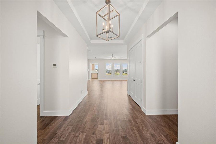 Hall with a chandelier, dark wood-type flooring, and a tray ceiling