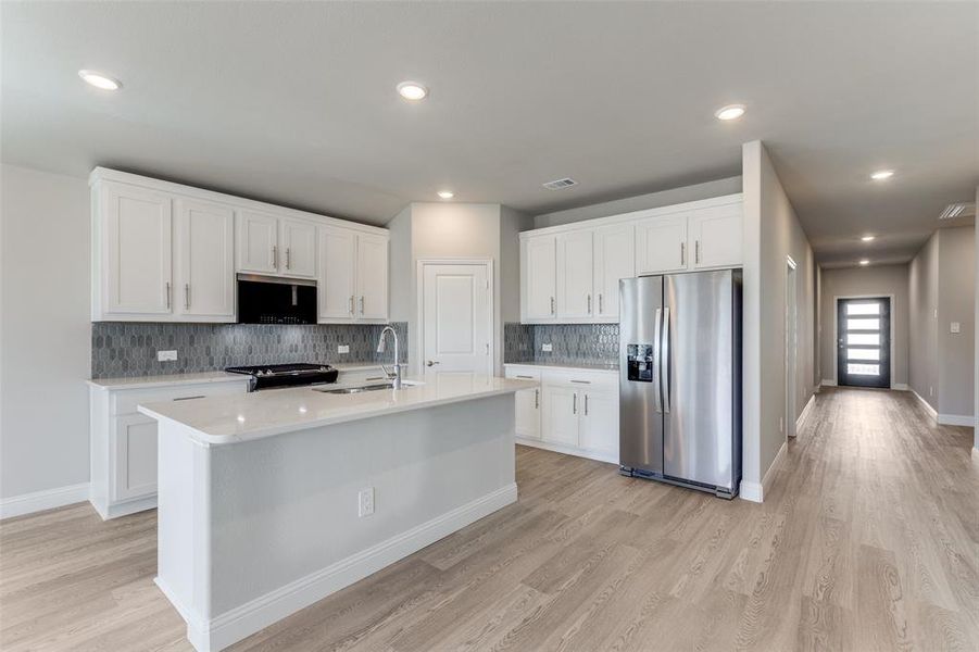 Kitchen with stainless steel appliances, white cabinetry, backsplash, light wood-style flooring, and a kitchen island with sink
